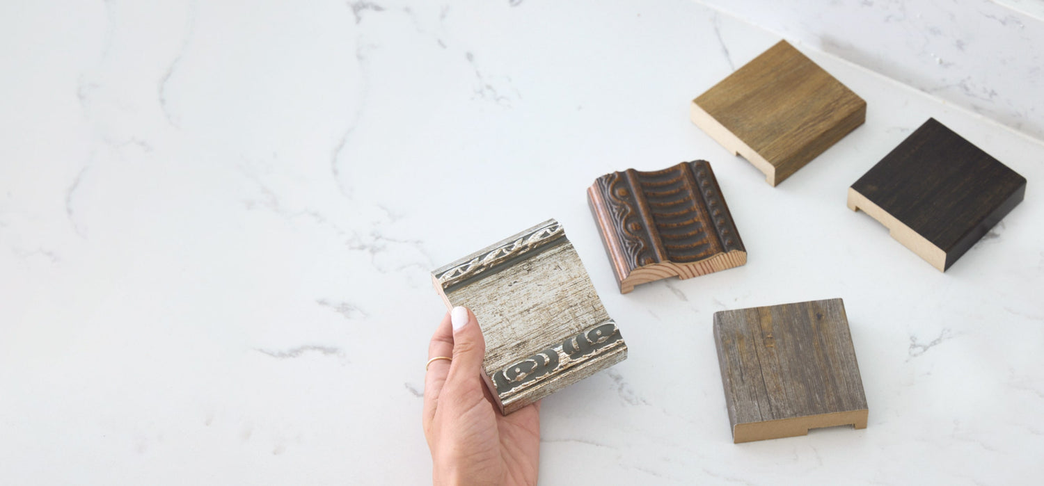 Hand holding a MirrorMate frame sample over a marble counter with four more samples
