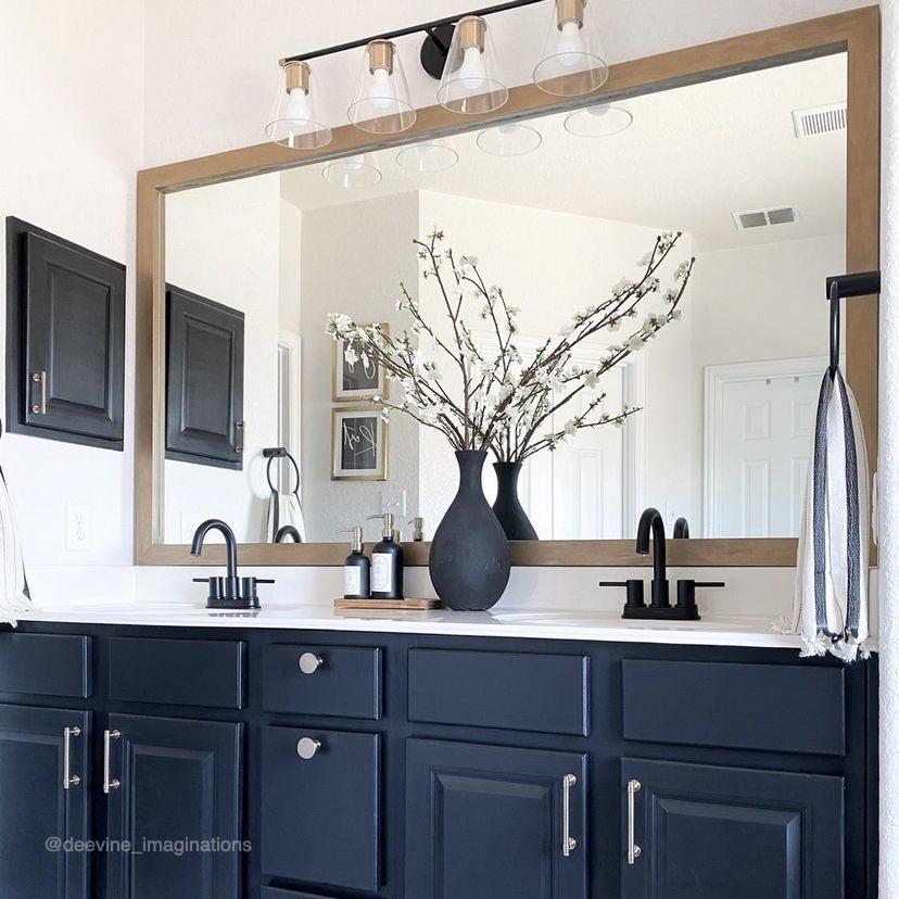 Bathroom with navy blue cabinets, large mirror with metallic mirror frame, and decorative elements.